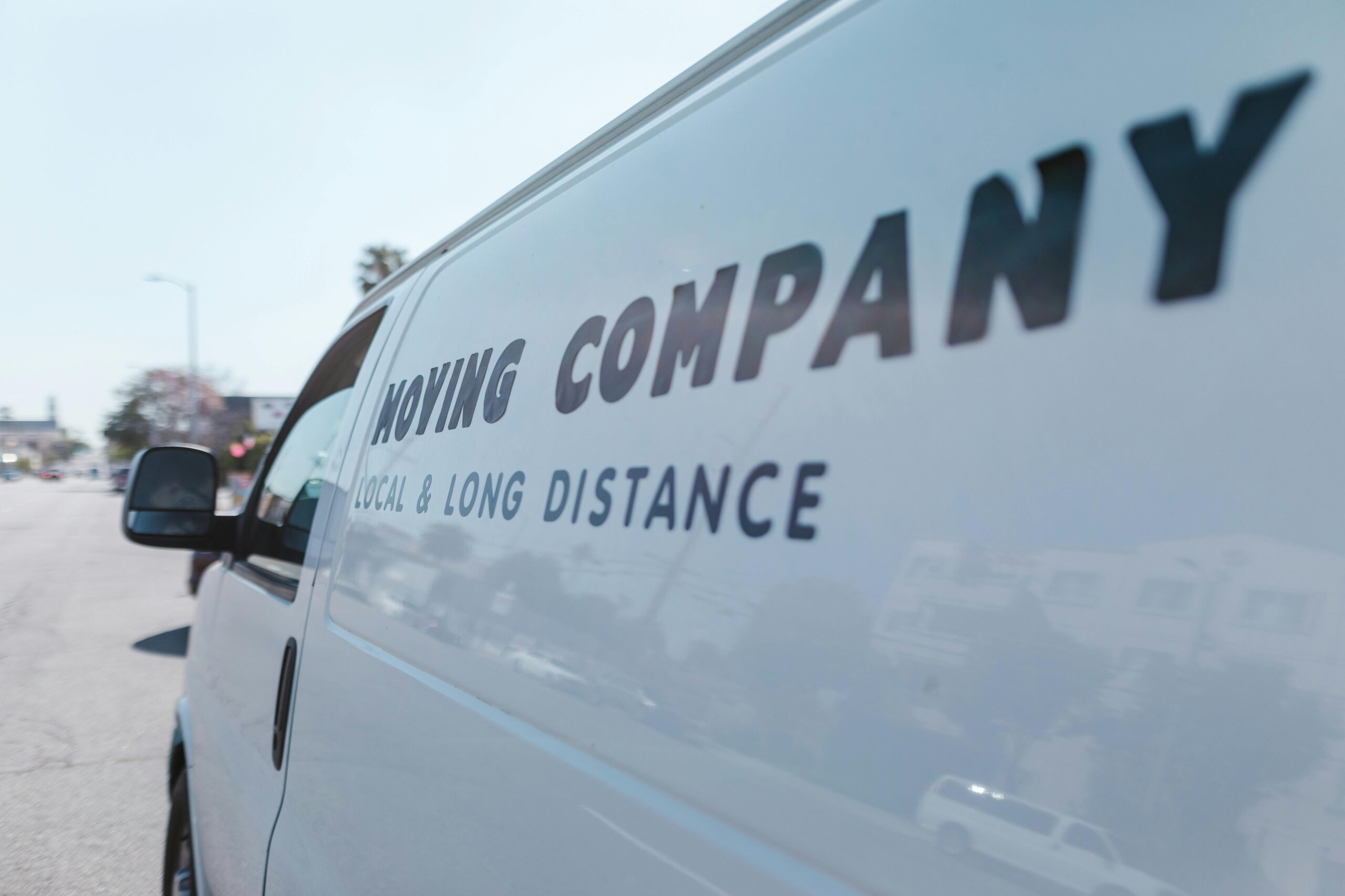 Close-up of a white moving company van with text on a sunny day street.